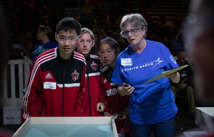 A team watching anxiously for their device to cross the finish line while a volunteer judge looks on.